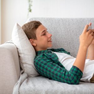 Side view of happy teenager playing games on mobile phone